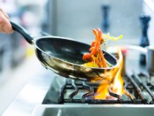 Chef in restaurant kitchen at stove with pan, doing flambe on fo